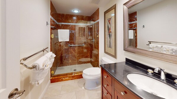 A modern bathroom with a marble shower, a white toilet, a sink with a black countertop, and a large mirror. - House Of The Sun #503GS (Sarasota)