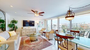 A modern living room with a flat-screen TV, a ceiling fan, and a dining area with a glass table.