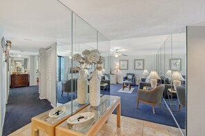 A spacious living room with a glass partition, a wooden bench, and a variety of seating options including a chair and a sofa. - House Of The Sun #414GF (Sarasota)
