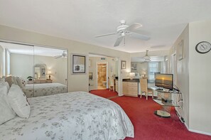 Une chambre d’hôtel équipée d’un lit, d’un bureau, d’une chaise, d’une télévision, d’une horloge et d’un ventilateur de plafond.