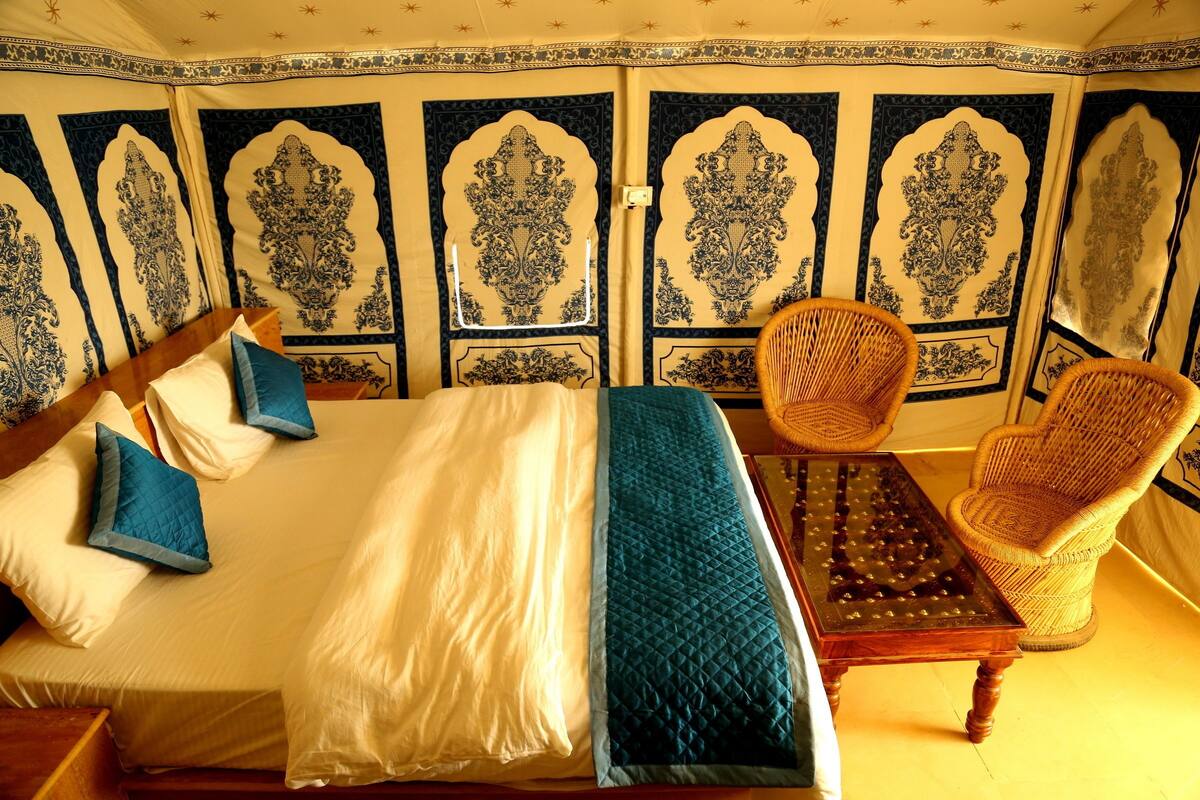 Una habitación con una cama grande, dos sillas y una mesa. Las paredes presentan intrincados diseños azules y blancos.