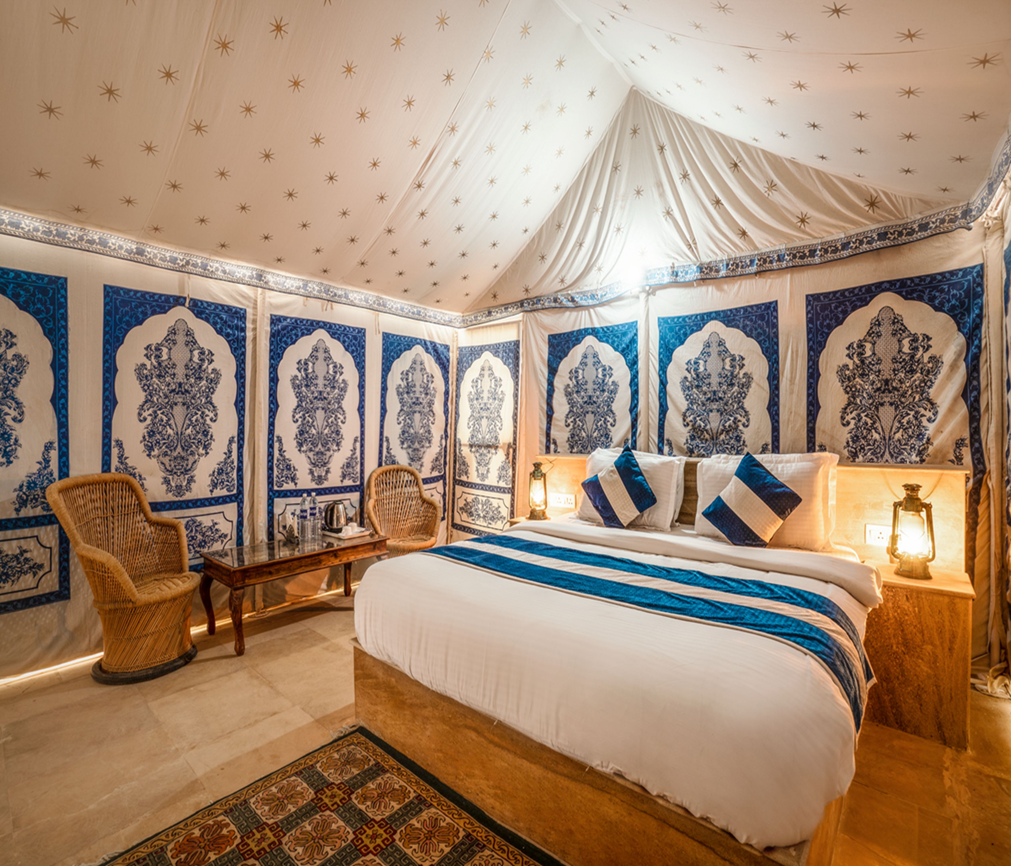 A room with a large bed, two chairs, a nightstand, and a patterned rug.