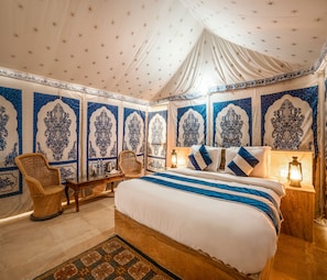 Una habitación con una cama grande, dos sillas, una mesita de noche y un tapete estampado.