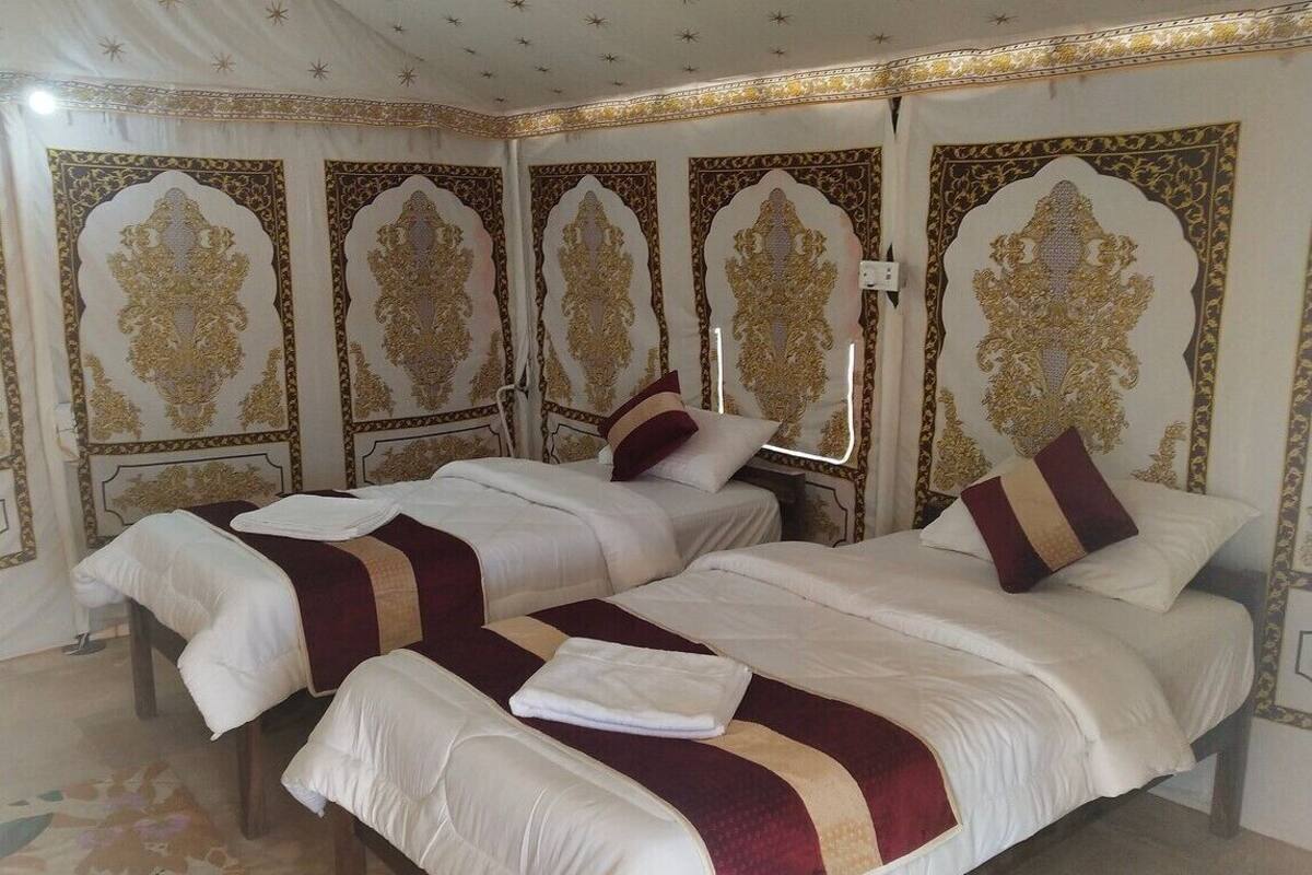 Una habitación de hotel con tres camas, cada una con ropa de cama blanca y burdeos, y elaborados diseños de cabeceros dorados.
