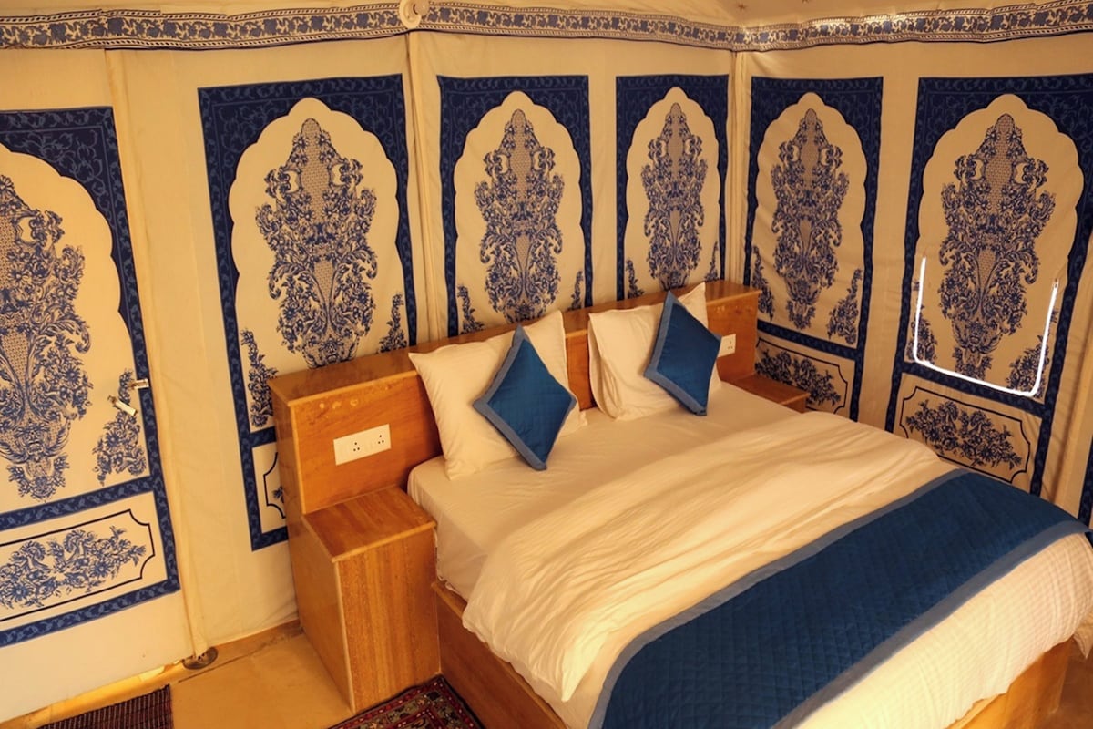 A bedroom with a wooden bed, blue pillows, a patterned rug, and ornate wall decorations.