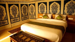Quarto tradicional com uma cama grande, paredes estampadas e uma pequena mesa.