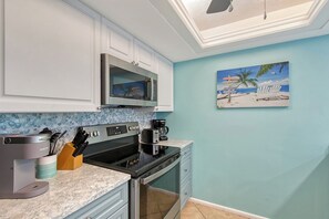A kitchen with white cabinets, a microwave, a coffee maker, and a painting of a beach scene.
