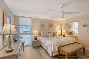 A bedroom with a bed, bedside tables, a chair, a desk, a lamp, a ceiling fan, and a window.