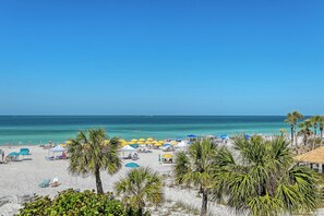 A beach with umbrellas, palm trees, and a clear sky.