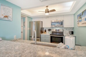 A kitchen with a marble countertop, stainless steel appliances, and a ceiling fan. - House Of The Sun #316GF (Sarasota)