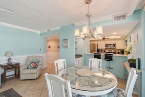 A modern kitchen with stainless steel appliances, a dining area with a glass table, and a living room with a sofa and decorative pillows.