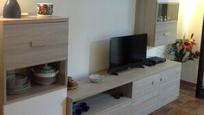 Un salon moderne avec un téléviseur à écran plat posé sur un meuble en bois, un vase et des objets décoratifs sur des étagères.
