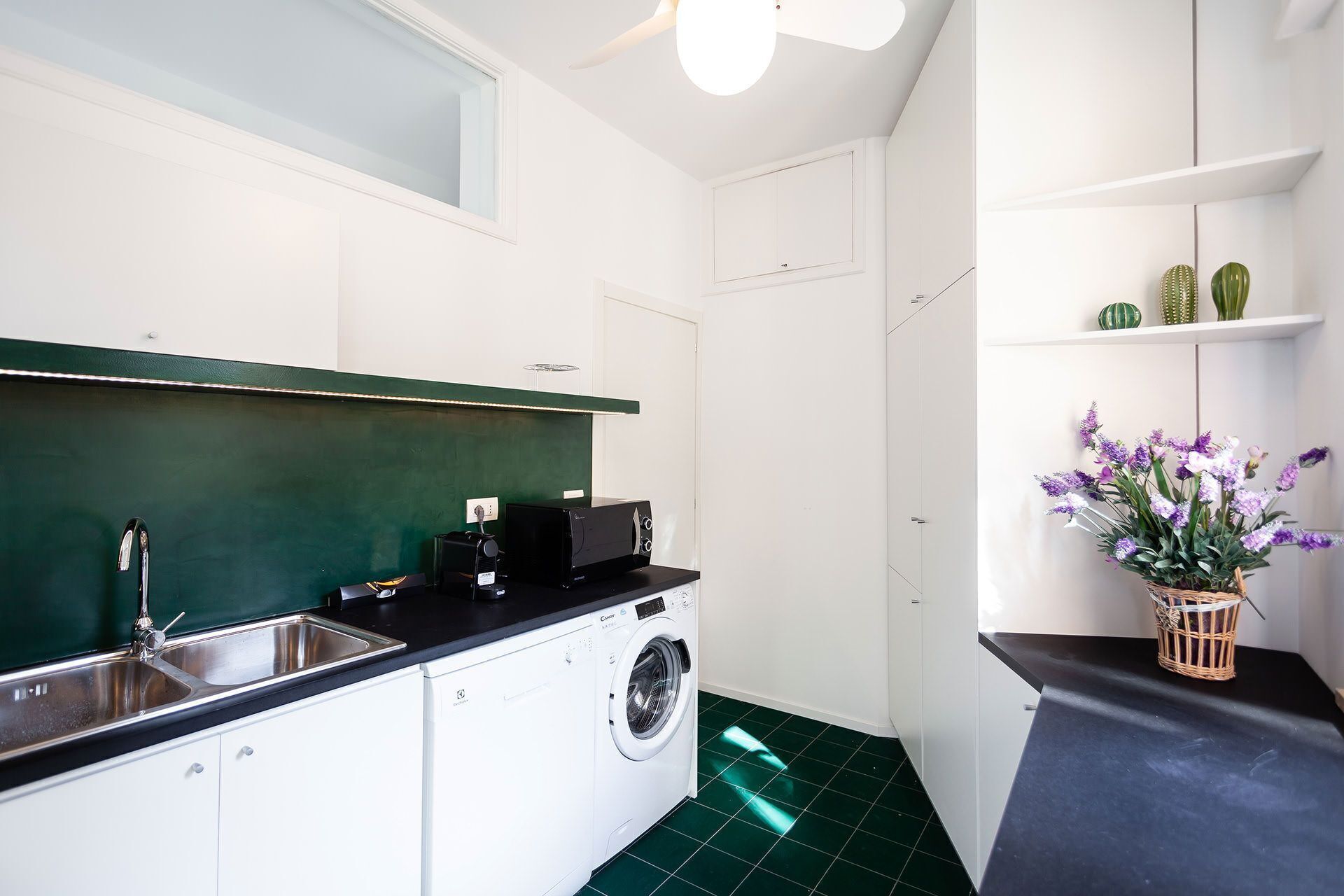 Une cuisine compacte équipée d’un lave-linge, d’un évier et d’un plan de travail.