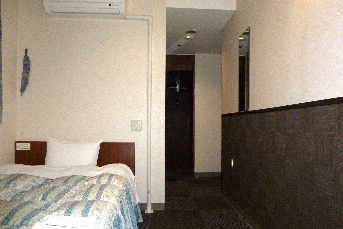 A hotel room with a bed, a nightstand, a mirror, and a door leading to another room.