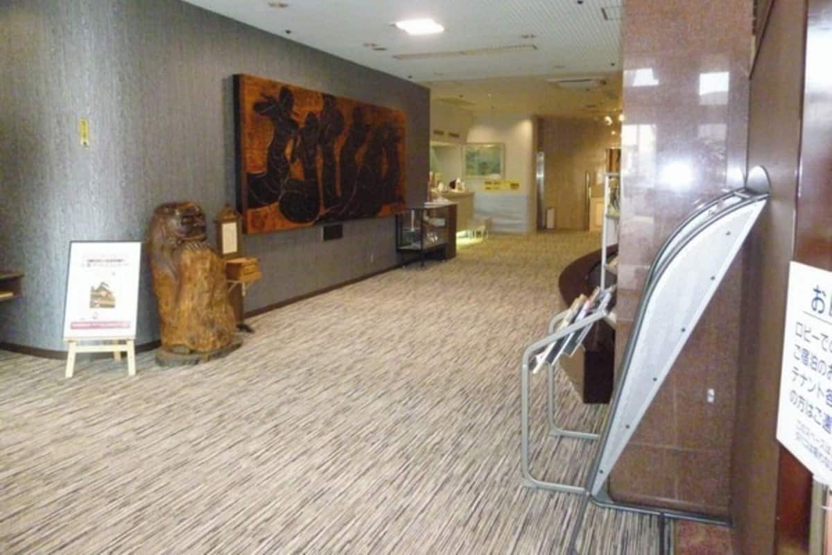 A hotel corridor with a large abstract painting on the wall, a wooden sculpture, and a signboard.