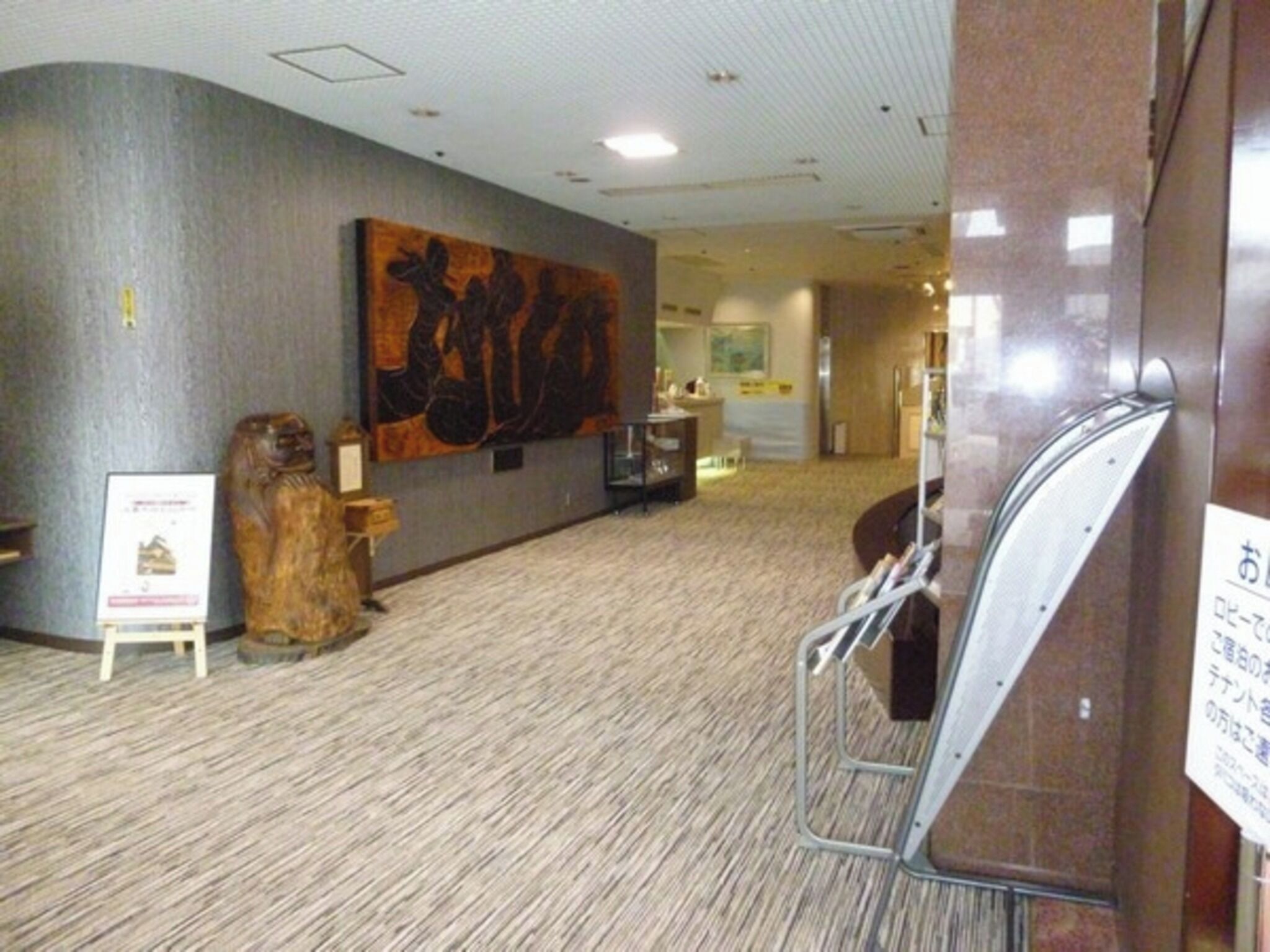 A hotel corridor with a large abstract painting on the wall, a wooden sculpture, and a signboard.