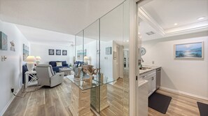 A modern living room with a glass partition, a dining area with a view, and a kitchen with a clock on the wall. - House Of The Sun #303GS (Sarasota)
