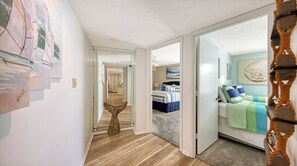 A hallway leading to a bedroom with a bed, a wooden stool, and artwork on the walls.