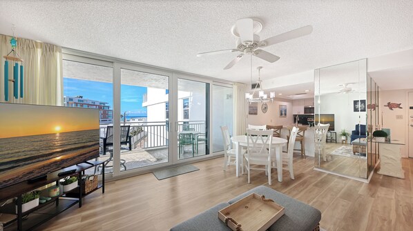 A modern living room with a large TV, a dining area, and a kitchen.