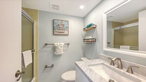 A bathroom with a shower, toilet, sink, and a large mirror. - House Of The Sun #303GS (Sarasota)