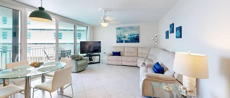 A modern living room with a glass dining table, sofa, and a ceiling fan.