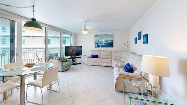 A modern living room with a glass dining table, sofa, and a ceiling fan. - House Of The Sun #312GV (Sarasota)