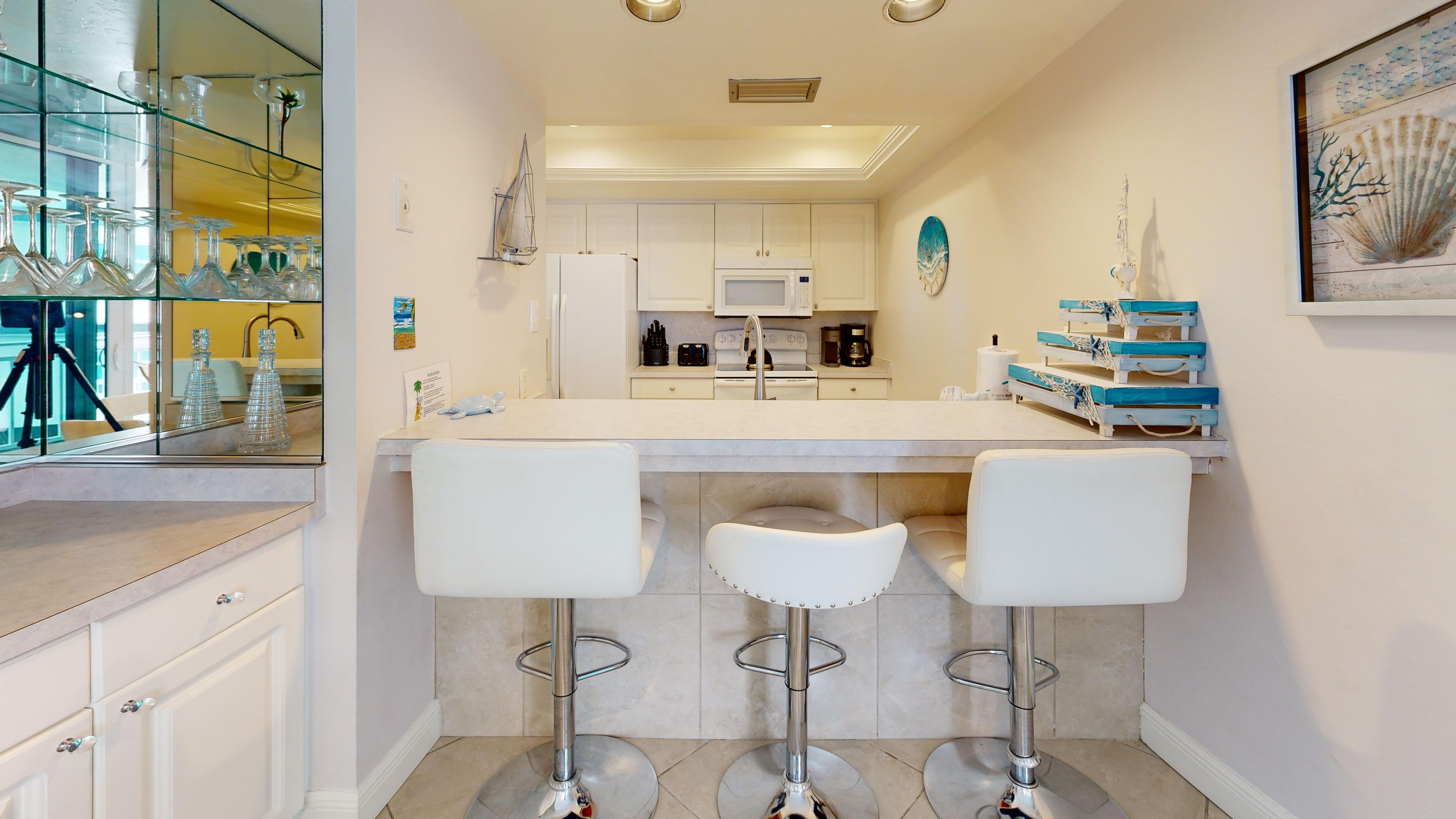 A modern kitchen with a central island, bar stools, and a glass display case.