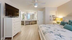 A bedroom with a bed, a vanity with a mirror, a television, and a ceiling fan. - House Of The Sun #312GV (Sarasota)