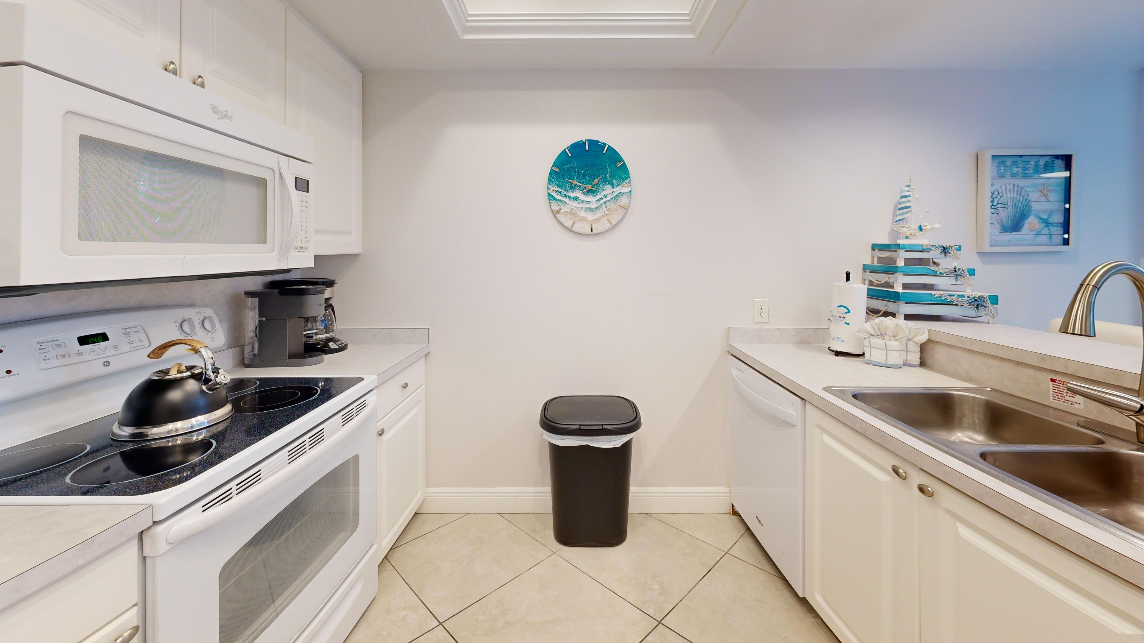 A modern kitchen with white cabinetry, a microwave, a kettle, a coffee maker, a trash bin, and a sink.