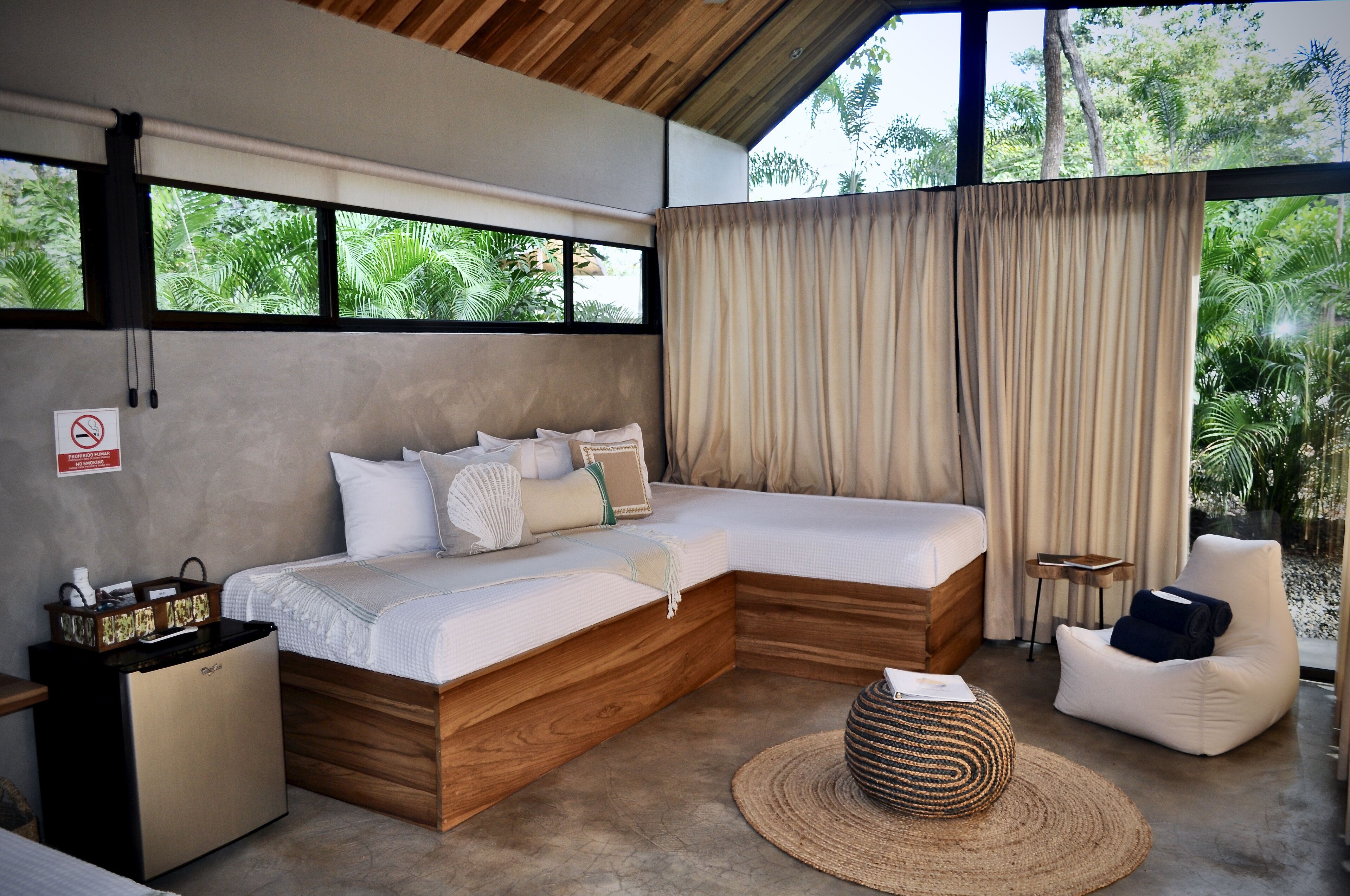 A modern bedroom with a large bed, a small sofa, a chair, and a compact refrigerator.