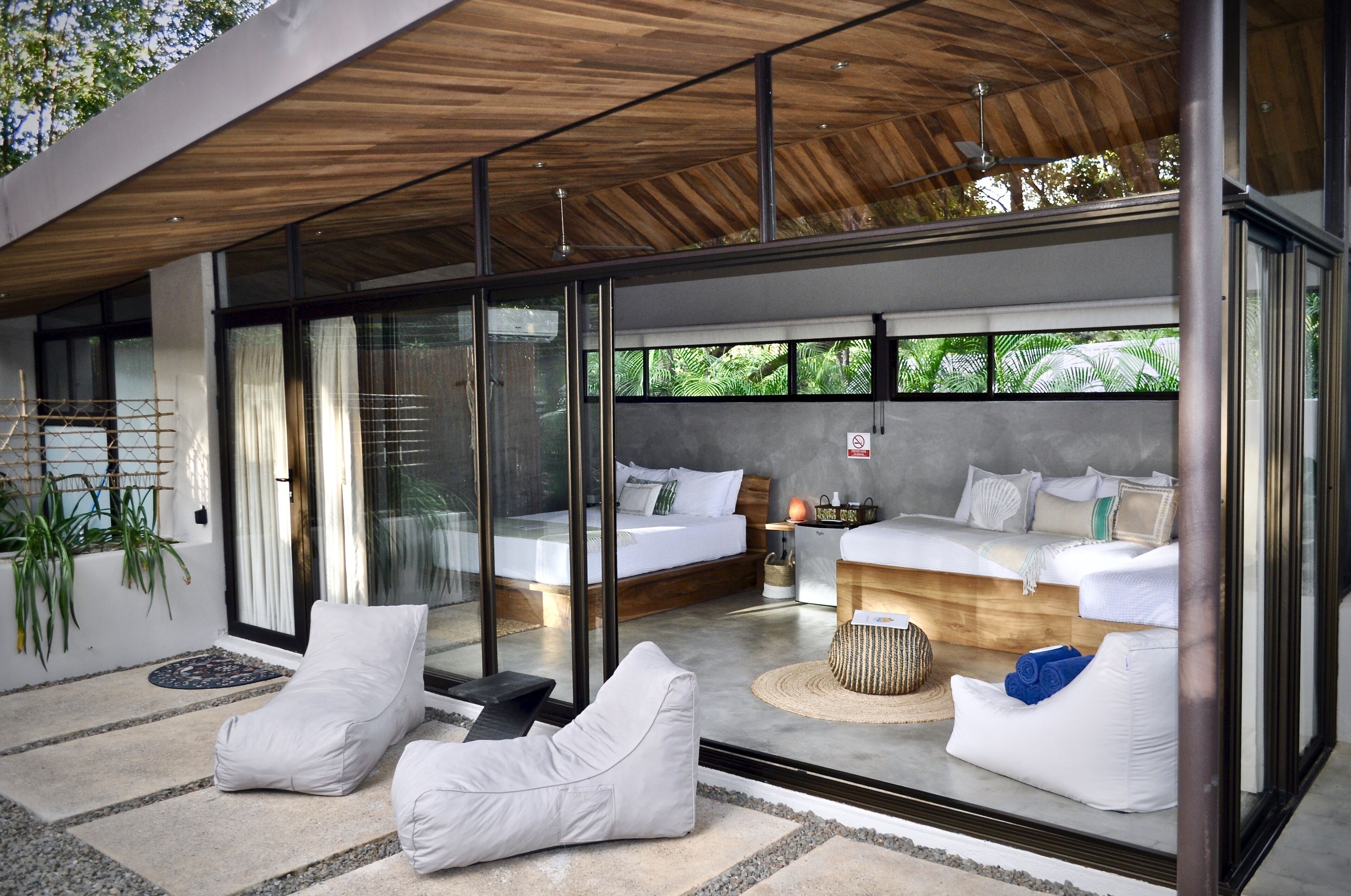 A modern bedroom with a glass wall, two beds, and a seating area with white cushions.