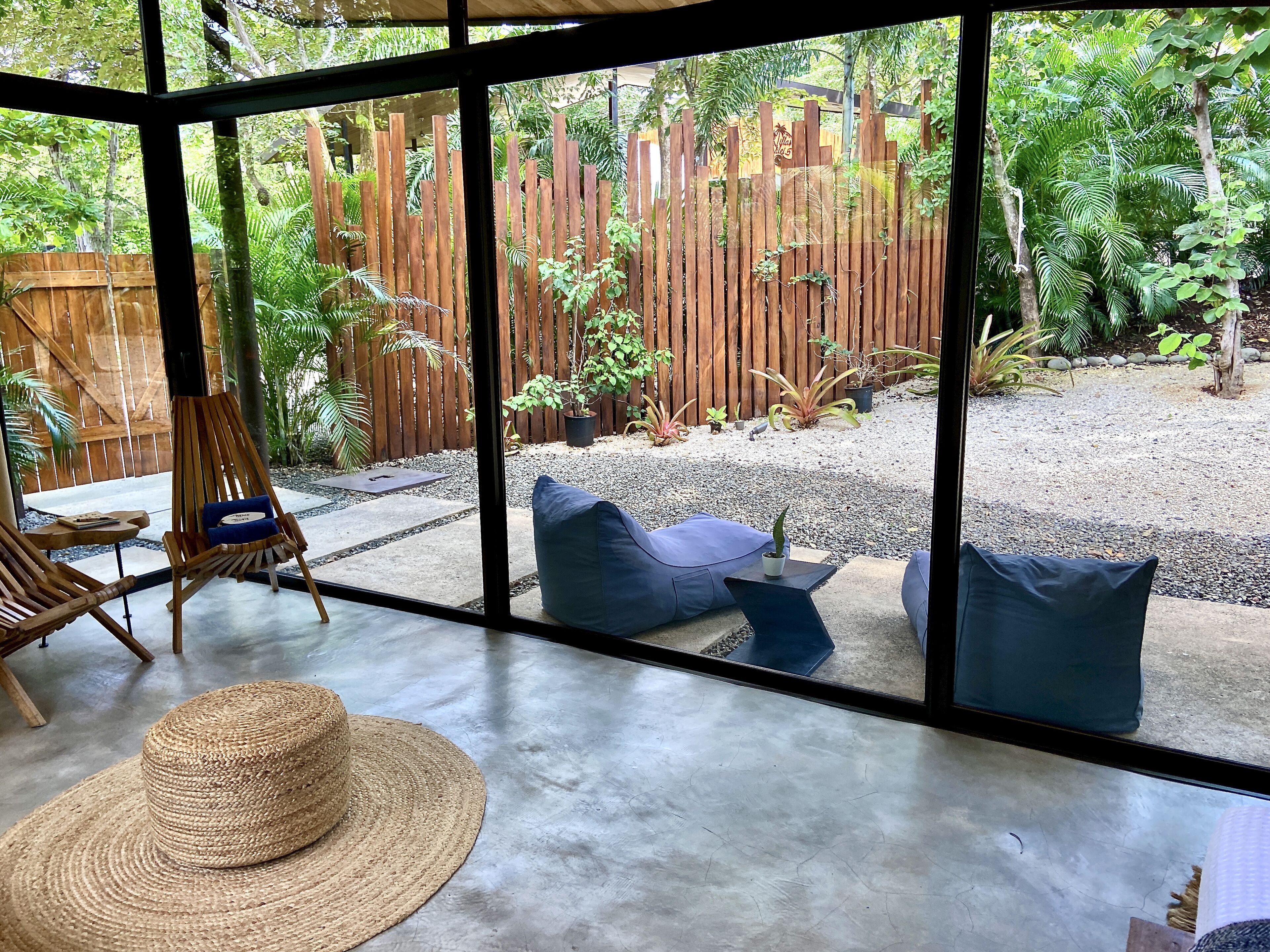 A room with a large window overlooking a garden with a wooden fence, outdoor seating, and a hat on the floor.