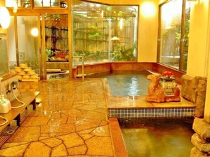 A traditional Japanese onsen with a stone floor, a small hot spring, and a wooden statue. - Chuo Hotel (Chikuma)