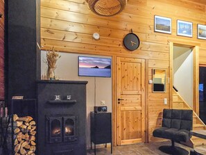 A cozy cabin interior with a fireplace, a television mounted on the wall, and a wooden door.