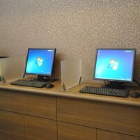 Two desktop computers with keyboards and mice on a wooden desk against a textured wall.