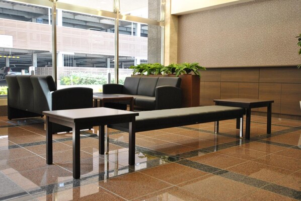 A modern waiting area with seating, a coffee table, and a large window offering a view of the parking garage. - Hotel Mark 1 Tsukuba (Tsukuba)