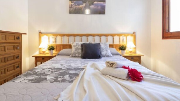 Un lit bien fait, recouvert d’une couvre-lit à motifs floraux, avec deux lampes de chevet, une tête de lit en bois et un tableau accroché au-dessus du lit.