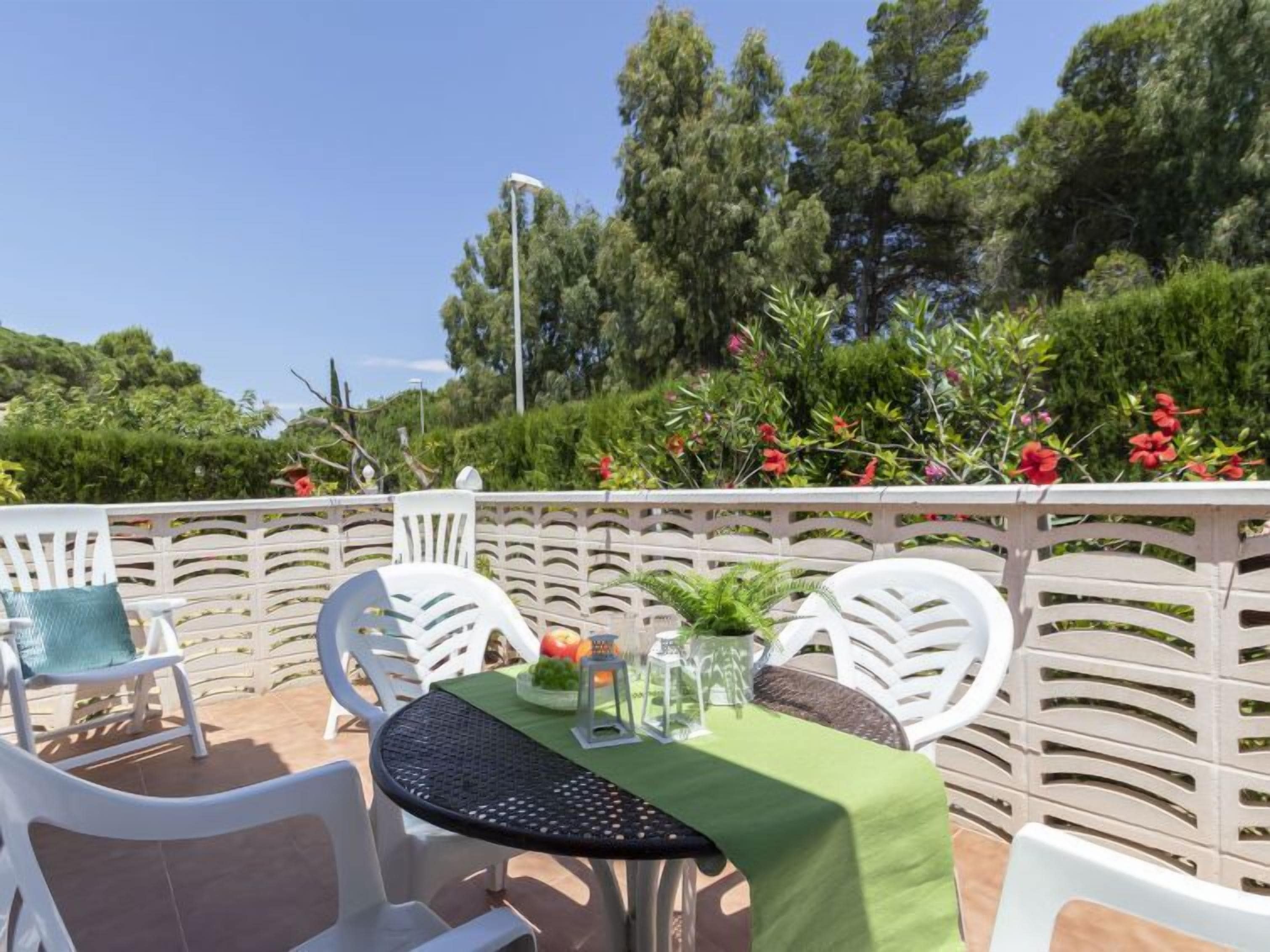 Eine Terrasse im Freien mit weißen Stühlen und einem Tisch, der mit einer grünen Tischdecke bedeckt ist, umgeben von einem weißen Zaun und üppigem Grün.