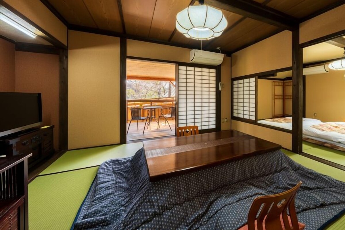 A traditional Japanese-style room with tatami flooring, a low wooden table, a futon bed, and sliding shoji doors.