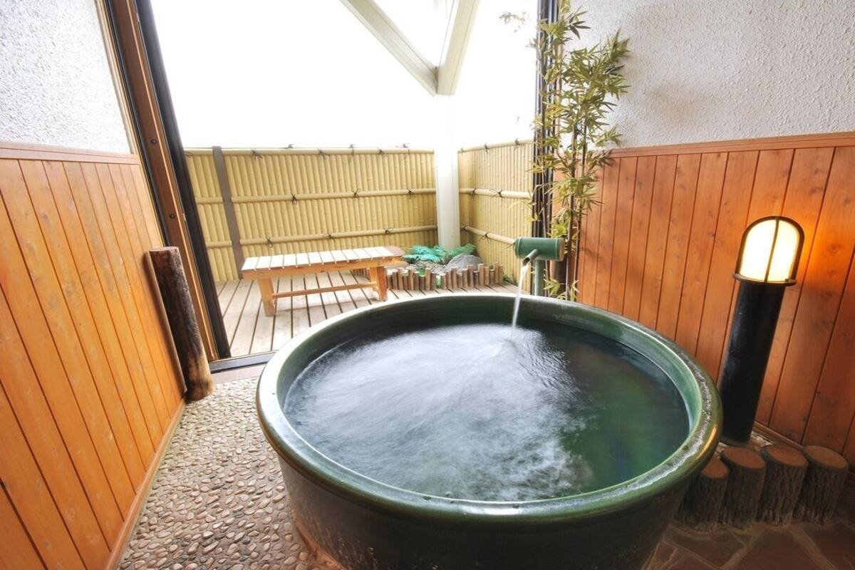 A hot tub with a wooden bench and a bamboo fence in the background.