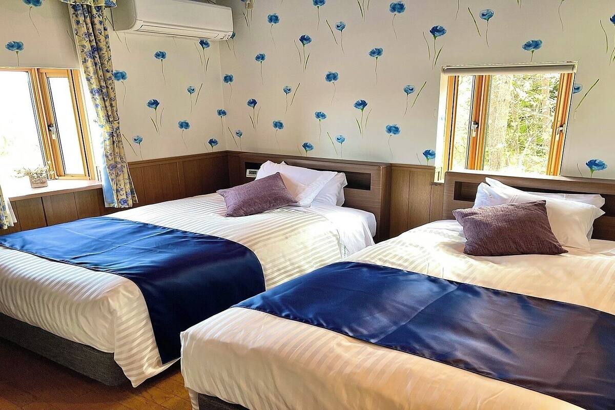 A hotel room with two beds, a window, and a floral wallpaper pattern.