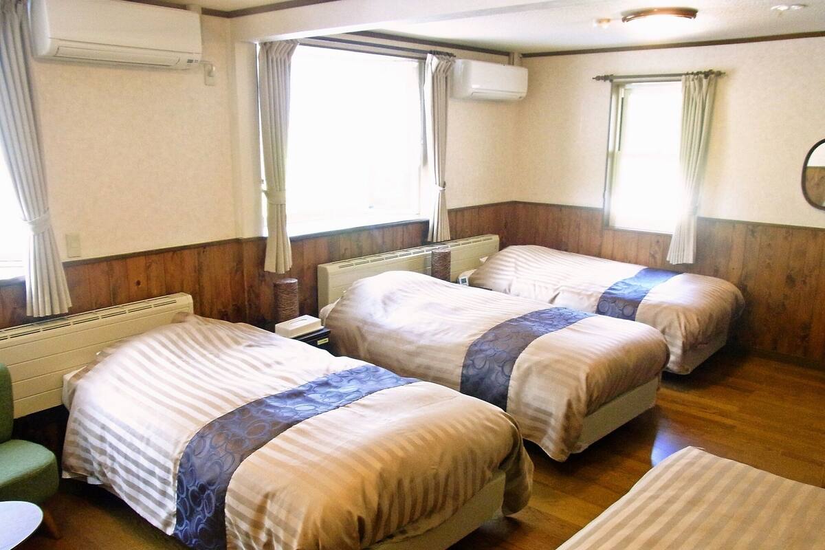 A hotel room with two beds, a radiator, a small table, and a window with curtains.