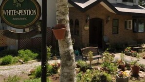 Un edificio con un letrero que dice 'WHITE-PENTION INAVASHIRO' y un jardín con plantas en macetas y un banco.