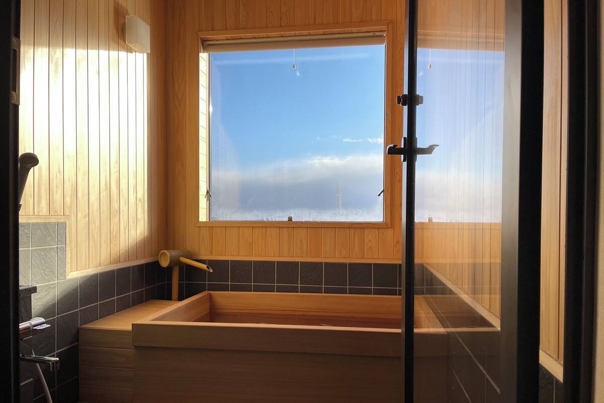 A modern bathroom with a wooden bathtub, a window with a view, and a shower area.