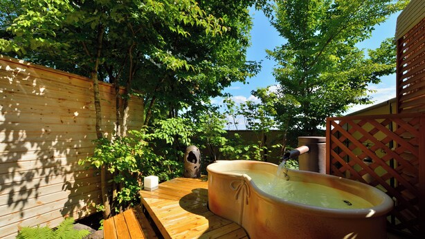 Una terraza de madera con un jacuzzi, rodeada de vegetación y un cerco de madera.