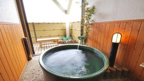Baño de aguas termales con un banco de madera y una cerca de bambú al fondo.