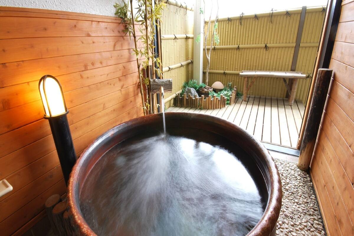A hot spring bath with a wooden wall and bamboo fence in the background.