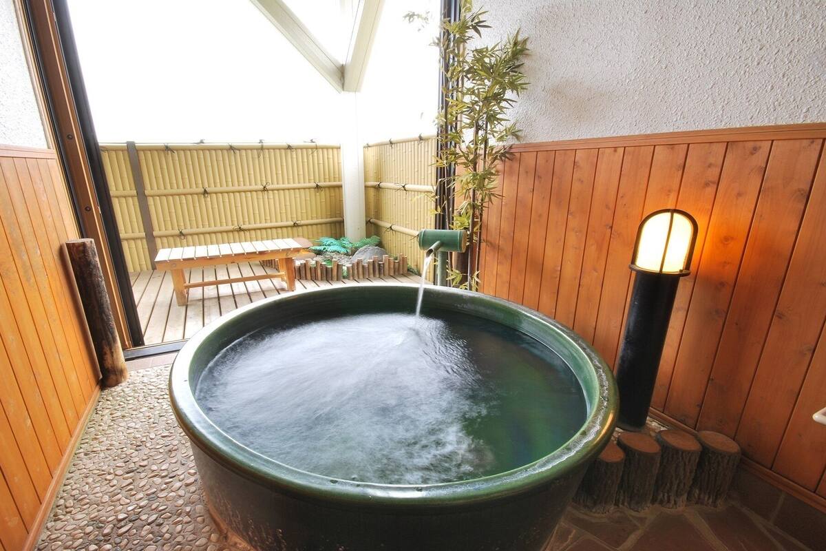 A hot spring bath with a wooden bench and a bamboo fence in the background.