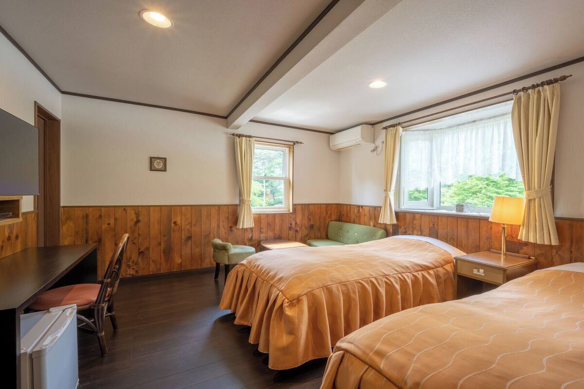 A hotel room with two beds, a desk, a chair, and a window with curtains.
