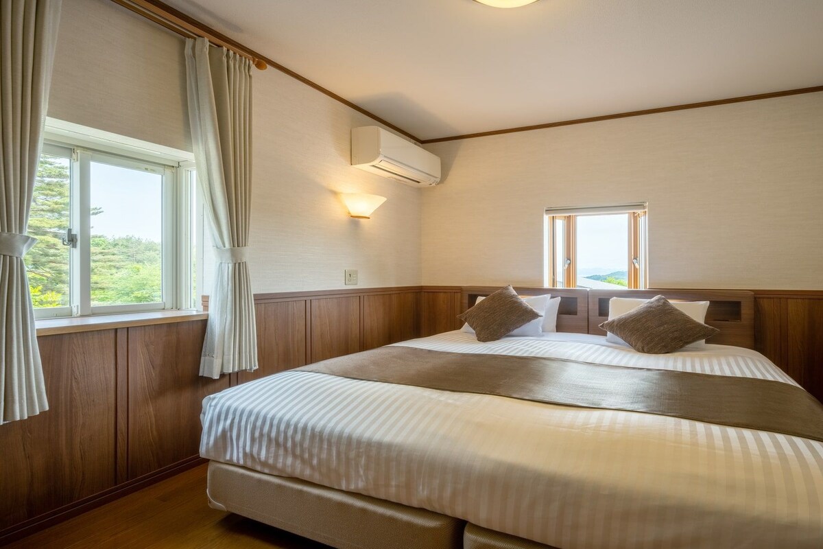 A hotel room with a large bed, a window with curtains, an air conditioning unit, and a view of the outdoors.